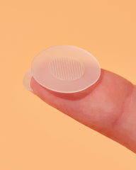 Clear microneedling patch on a finger against a peach background