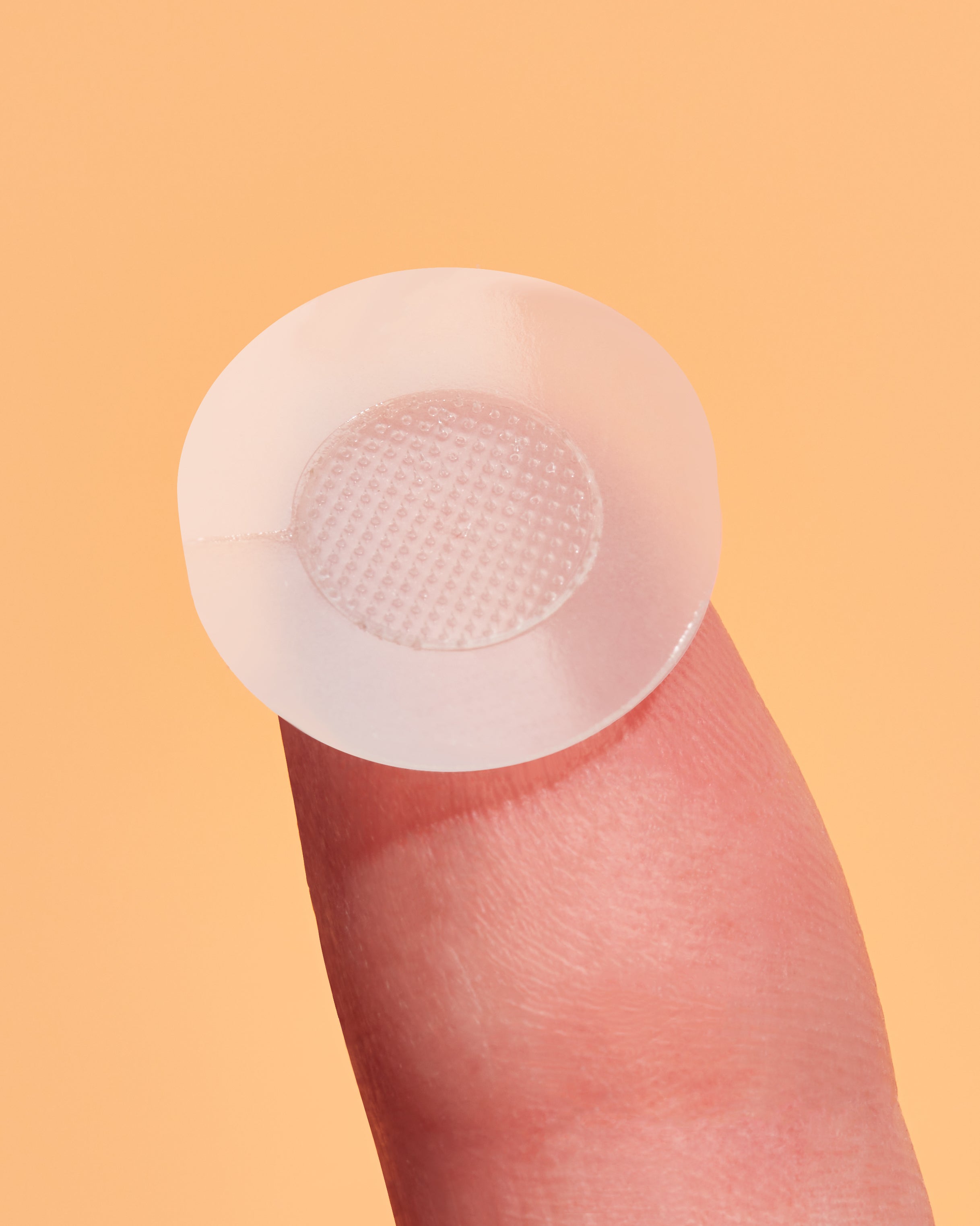 Clear microneedling patch on a finger against a peach background