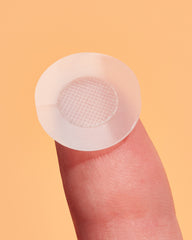 Clear microneedling patch on a finger against a peach background