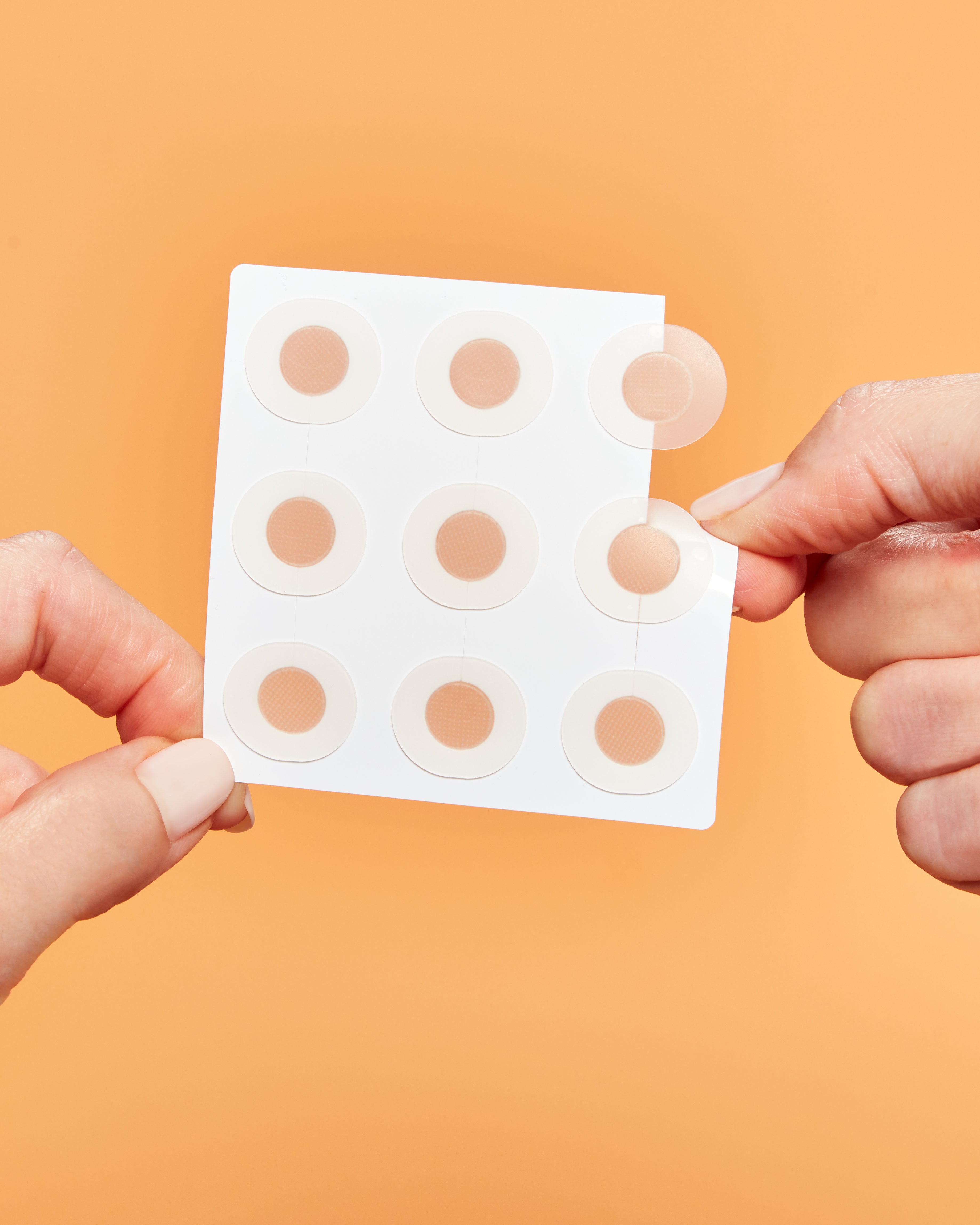 Hand holding a sheet of microneedling dark spot patches against an orange background
