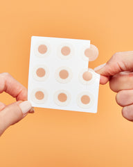 Hand holding a sheet of microneedling dark spot patches against an orange background