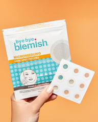 Hand holding 'bye bye blemish' microneedling dark spot patches against an orange background