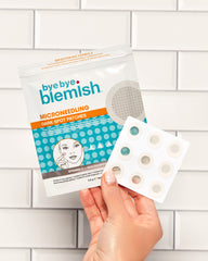 Hand holding a package of 'bye bye blemish' microneedling dark spot patches against a tiled wall background.