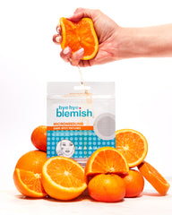Hand squeezing an orange with 'bye bye blemish' microneedling dark spot patches and oranges on a white background